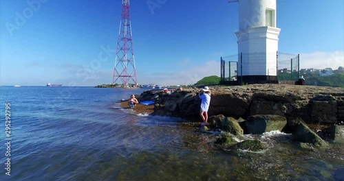 Aerial view of woman taking photo of man with little son at Tokarevsky lighthouse, one of the most importrant attactions in Vladivostok, Russia. Nice sunny summer day photo