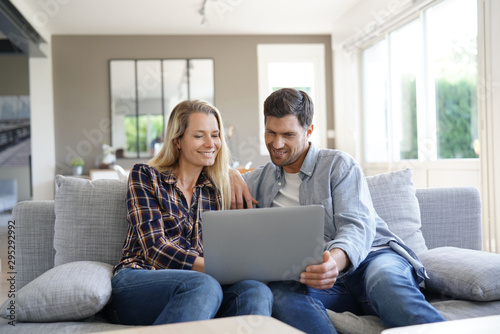 Cheerful couple at home using laptop