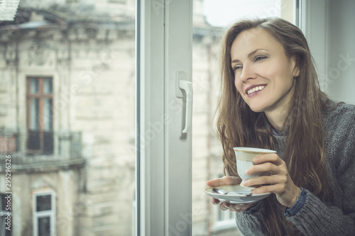 Beautiful woman drinking  tea or coffee by the window