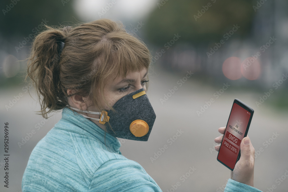 Plakat Kobieta nosząca prawdziwą maskę antysmogową i sprawdzająca aktualne zanieczyszczenie powietrza za pomocą aplikacji na smartfona