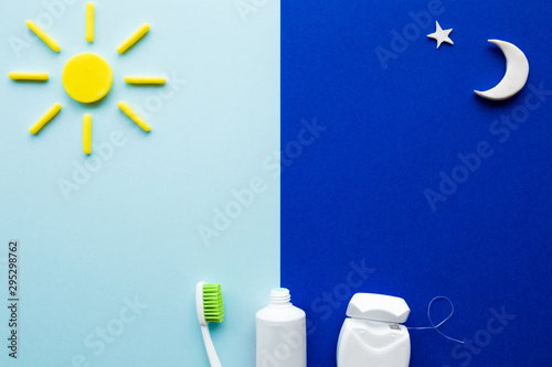 White toothbrush, tube of toothpaste and dental floss. Sun and moon on light and dark blue background. Care about teeth in morning and evening. Daily routine concept. Top down view.