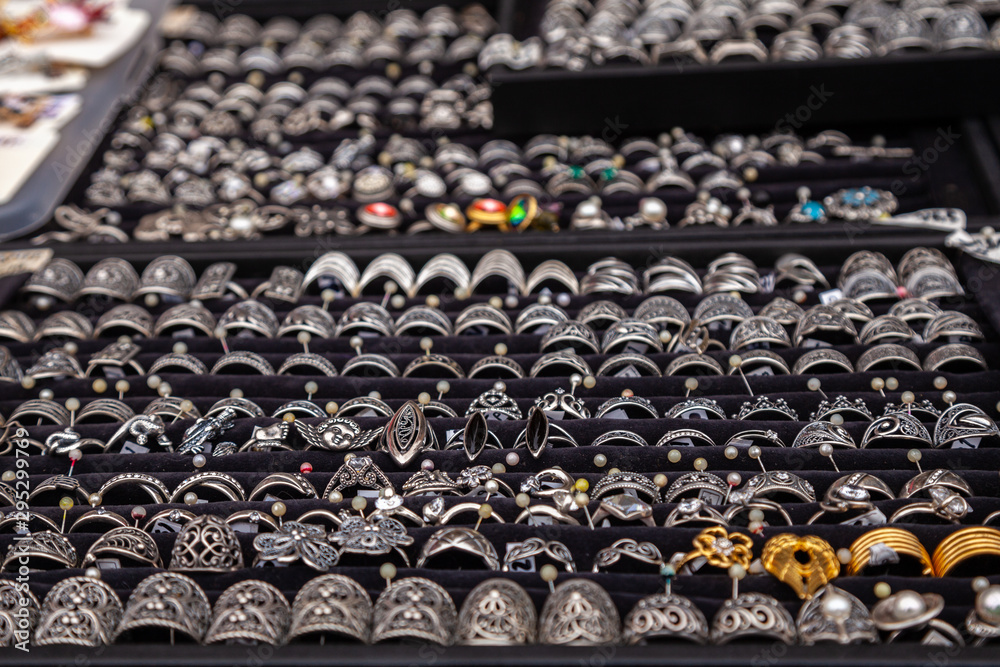 Fototapeta premium Silver rings with precious stones at the jewelry market exhibition. Selective focus. Silver rings and jewelry on a counter in a store.