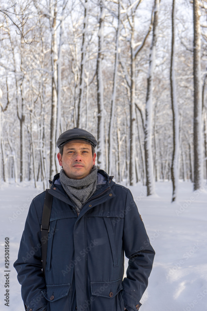 Portrait of handsome middle-aged man walking in winter snowy park or forest. Attractive man in jacket, scarf and cap looking at camera. Winter mood, authentic lifestyle concept, stylish male outfit Portrait of handsome middle-aged man walking in winter snowy park or forest. Attractive man in jacket, scarf and cap looking at camera. Winter mood, authentic lifestyle concept, stylish male outfit