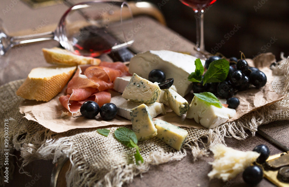 Assorted cheeses on wooden board. Camembert, cheese with blue mildew, gouda, hard cheese, strawberries, mint leaves, knives for cheese.