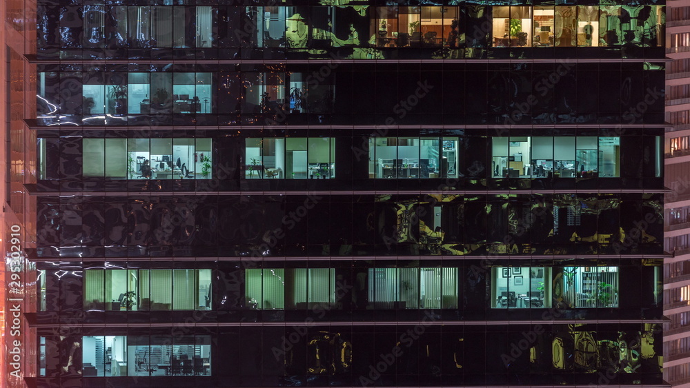 Office skyscraper exterior during late evening with interior lights on and people working inside night timelapse