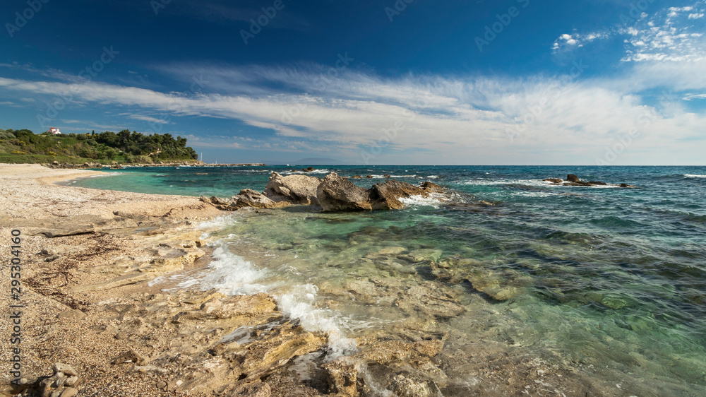 Big rocks and rocky coastline with clear green sea under a blue sky and white clouds at the west-coast of Central Greece