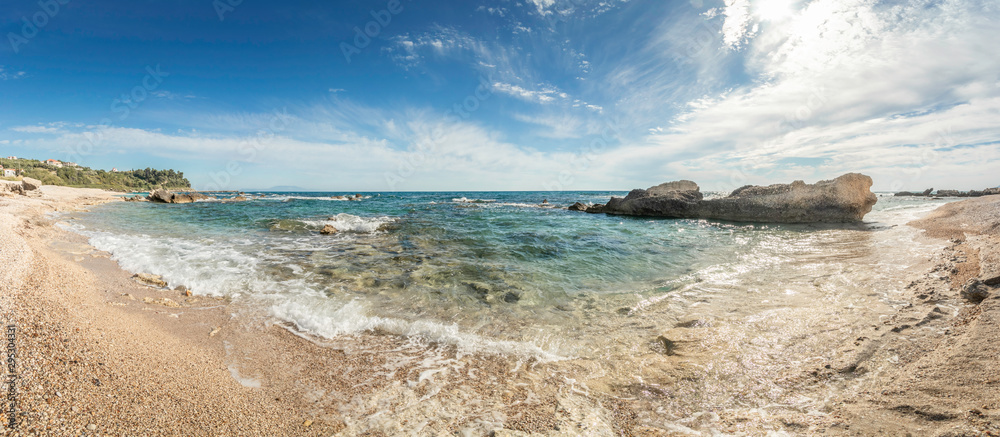 panorama of rocky coastline with clear green sea and sandy beach under a blue sky with some white clouds on the west-coast of Central Greece