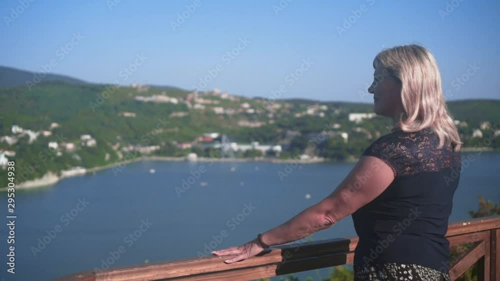 Pretty blonde woman walks at a height near a mountain lake with amazing views. A woman enjoys the view, seeing panoramic mountain views of the lake. Pretty blonde woman walks at a height near a mountain lake with amazing views. A woman enjoys the view, seeing panoramic mountain views of the lake.