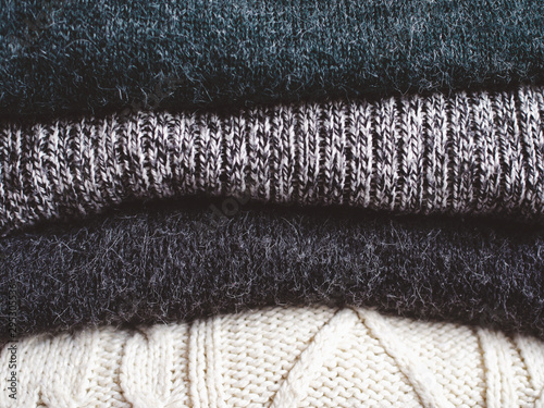 Pile of chunky winter sweaters laying on dark textured desk or table. photo