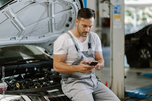 Mechanic reading a text message on smart phone in a workshop