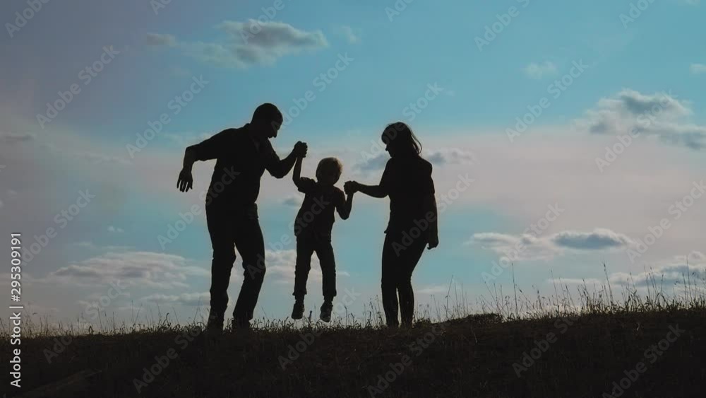 happy family father, mother and son outdoors silhouette concept slow motion video. dad man mom girl hold little lifestyle boy son by hands. little boy jumping silhouette at sunset outdoors. happy happy family father, mother and son outdoors silhouette concept slow motion video. dad man mom girl hold little lifestyle boy son by hands. little boy jumping silhouette at sunset outdoors. happy