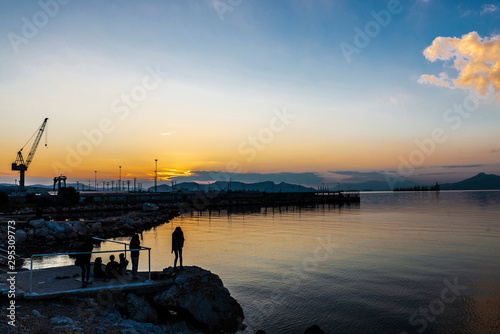 Backlight of children and harbor cranes at sunset in Greece