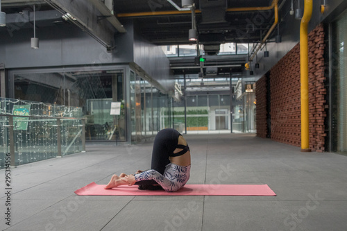 Young attractive smiling woman practicing yoga, sitting in One Legged King Pigeon exercise, Eka Pada Rajakapotasana pose, working out, wearing sportswear, grey pants, bra, indoor full length, home photo