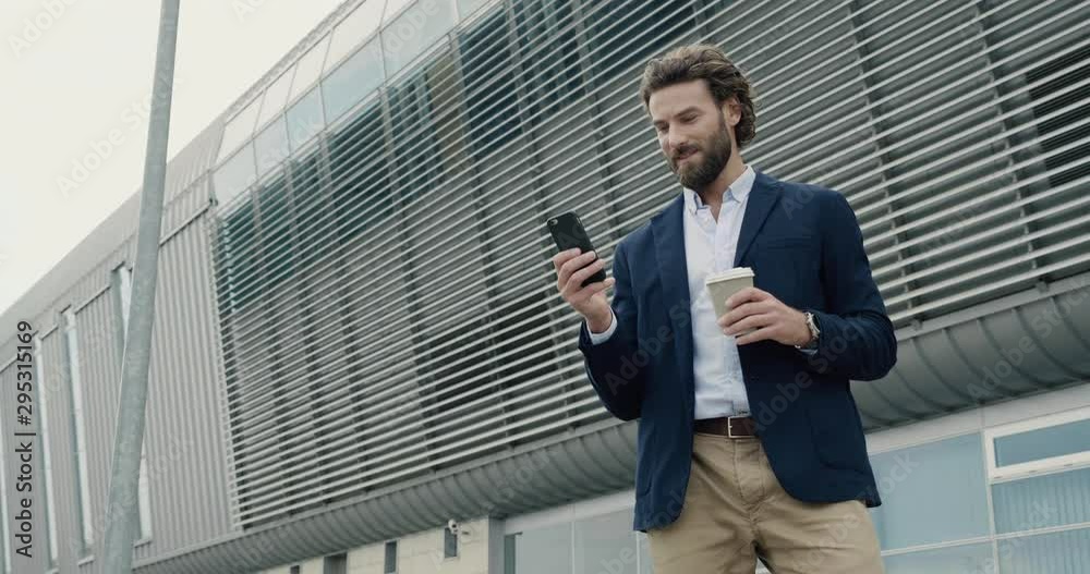 Smart casual dressed Office Worker drinking Coffe at the Break. Attractive Man is standing near modern big Office and browsing his Smartphone. Office Workers. People. Business. Phones. Smart casual dressed Office Worker drinking Coffe at the Break. Attractive Man is standing near modern big Office and browsing his Smartphone. Office Workers. People. Business. Phones.