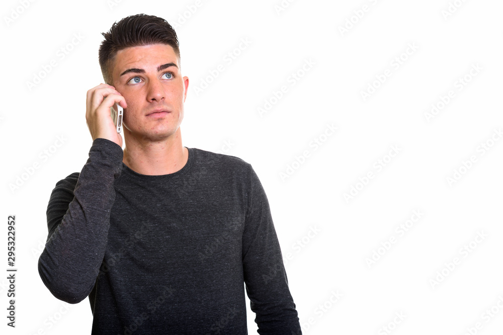 Studio shot of young handsome man talking on mobile phone while Studio shot of young handsome man talking on mobile phone while