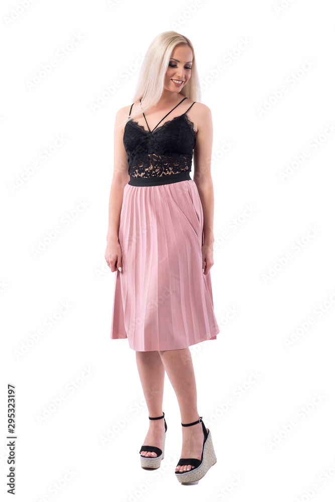 Attractive blonde young woman in elegant evening wear smiling and looking down. Full body isolated on white background. 