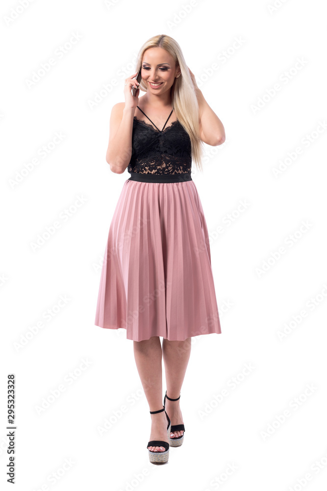 Carefree happy blonde young woman smiling while walking and talking on the cell phone. Full body isolated on white background. Carefree happy blonde young woman smiling while walking and talking on the cell phone. Full body isolated on white background.