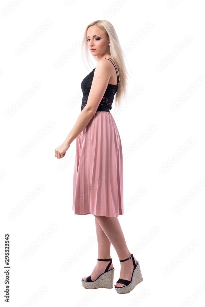 Glamour feminine blonde young woman in pink pleated skirt walking and looking down. Full body isolated on white background. Glamour feminine blonde young woman in pink pleated skirt walking and looking down. Full body isolated on white background.