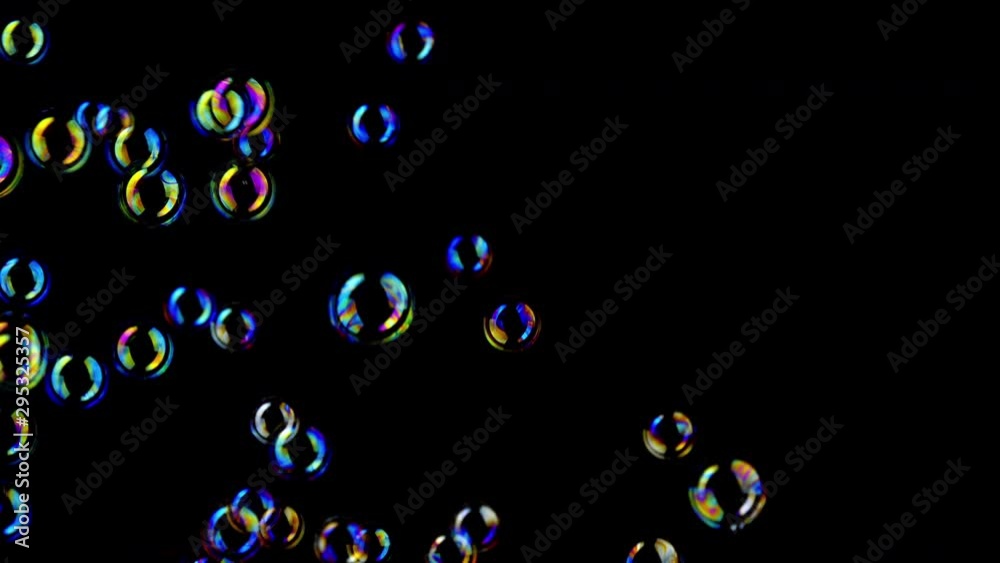 Colorful soap bubbles fly across black background. 