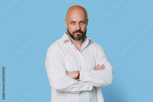 Serious middle-aged man with folded arms and a deadpan expression posing in front of a blue background © Nana_studio