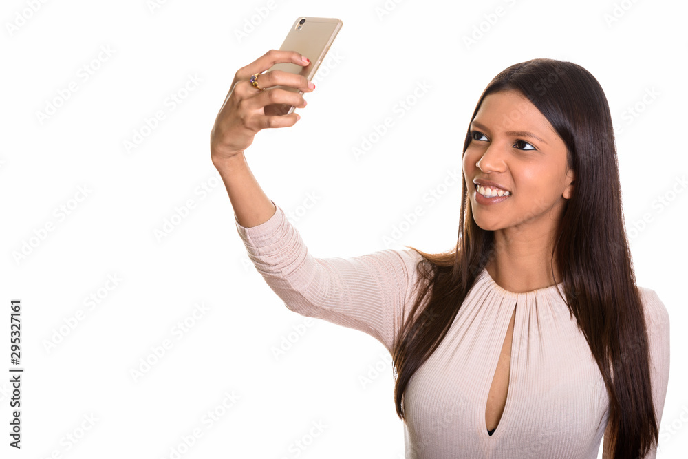 Studio shot of young happy Brazilian woman smiling while taking Studio shot of young happy Brazilian woman smiling while taking