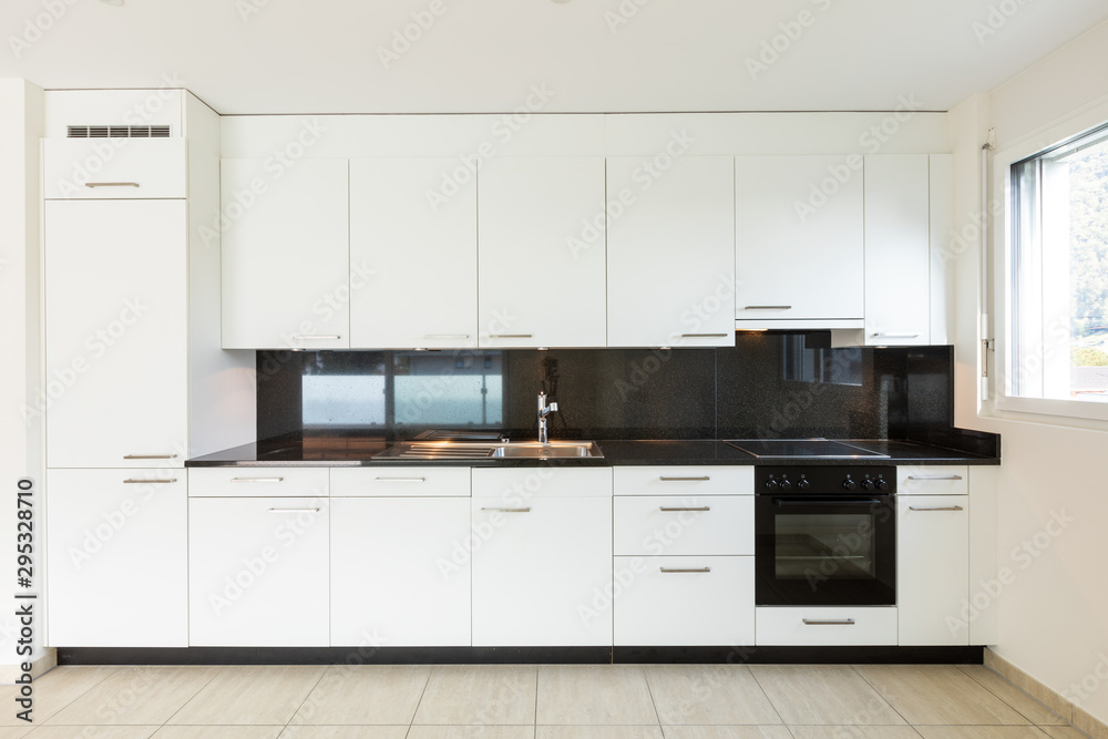 Empty room with white walls, travertine floor and white kitchen and black marble Empty room with white walls, travertine floor and white kitchen and black marble