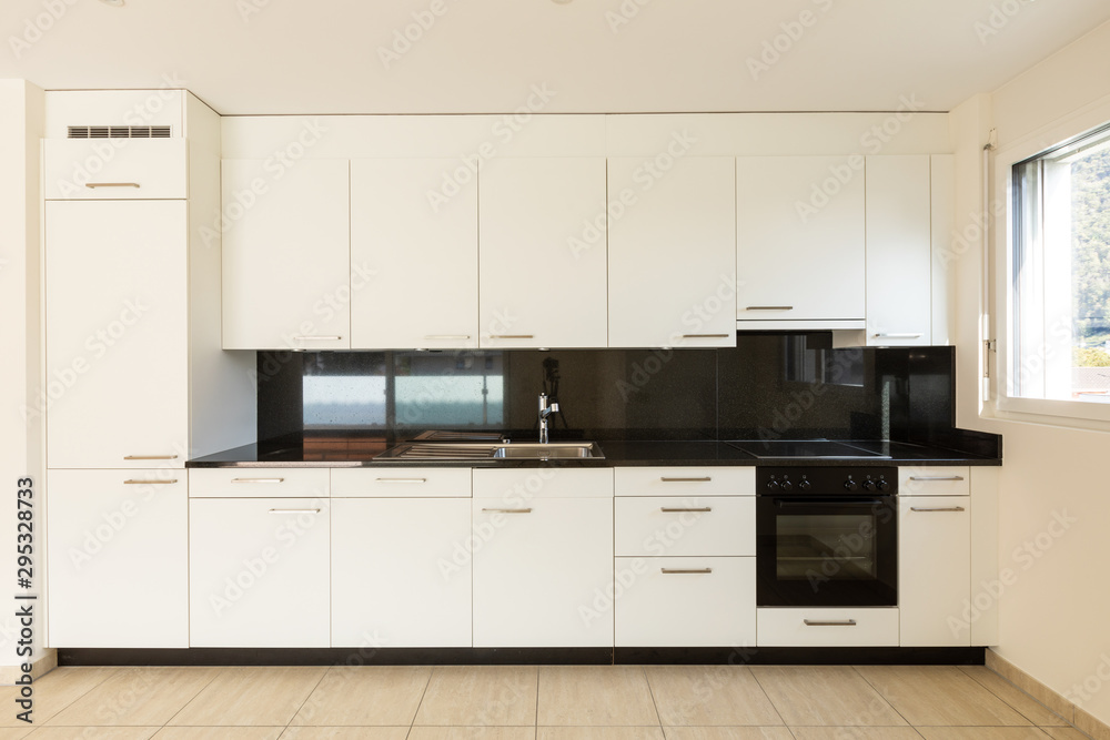 Fototapeta premium Empty room with white walls, travertine floor and white kitchen and black marble