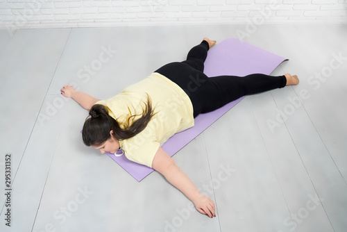 Fat girl lying on violet mat in star pose after training