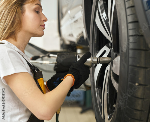 Side view of female mechanic changing tire of auto