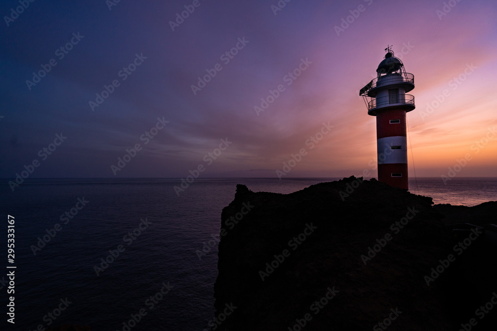  a lighthouse on the shore of the sea with the purple sky in the background