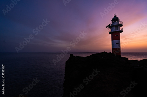  a lighthouse on the shore of the sea with the purple sky in the background