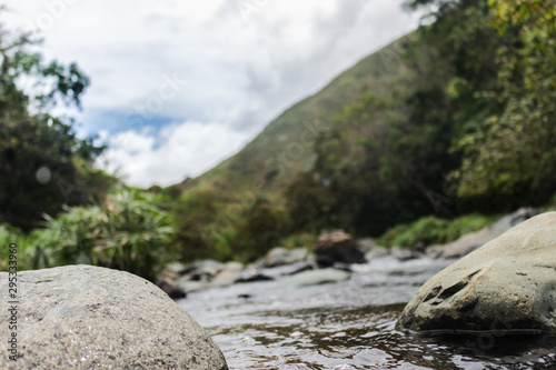 Photography of a beautiful river flowing through rocks, with mountains and trees in a blurred background.