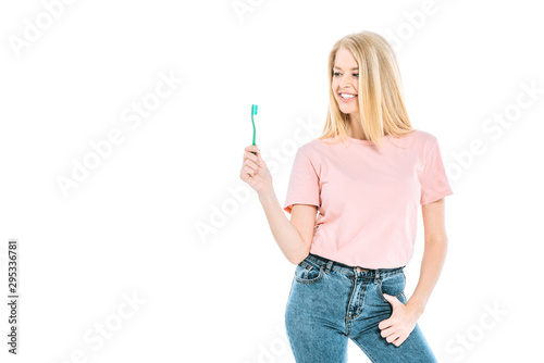attractive woman in blue jeans standing and looking at toothbrush isolated on white