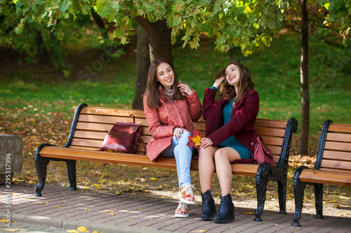 Two beautiful girls resting on a bench in the autumn park