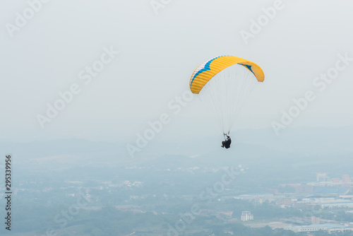Aerial photography of a yellow paraglider flying over the town in the smoggy weather