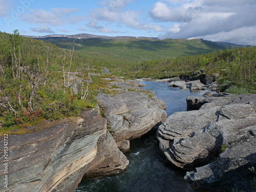 Blue glacial river canyon with granite rork boulders., birch tree forest and mountains. Abisko National Park, Lapland, Northern Sweden, at the start of Kungsleden trail. Summer sunny day photo