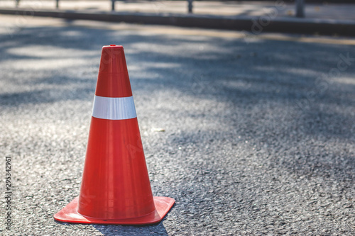 Red orange cone with a white stripe on the asphalt road. Drive safety and constructions concept.