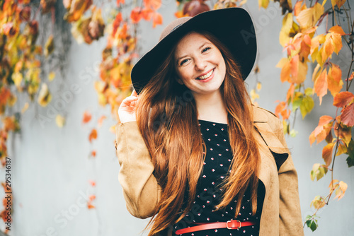 Pretty woman in hats with autumn leaves. The girl closing face the autumn leaf and having hun in the park. Concept of good mood at the autumn time.