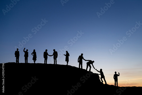 Silhouette of people helping each other hike up a mountain at sunset background. Teamwork, success and goal concept. © cofficevit