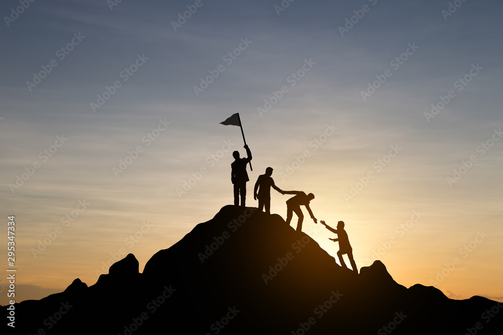Silhouette of people helping each other hike up a mountain at sunset background. Teamwork, success and goal concept.