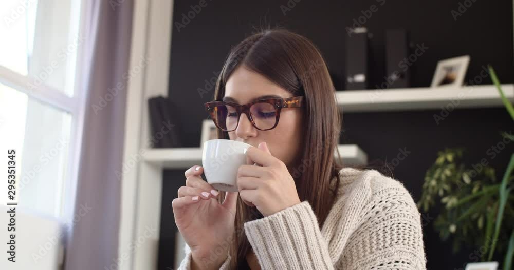 Caucasian woman dressed in beige sweater sitting on bed and holding fresh morning coffee. Caucasian woman dressed in beige sweater sitting on bed and holding fresh morning coffee.