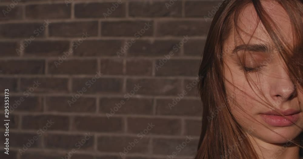 Close up of the half face of the young beautiful charming Caucasian woman, female model with eyes closed at the brick wall while wind waving her hair. Close up of the half face of the young beautiful charming Caucasian woman, female model with eyes closed at the brick wall while wind waving her hair.