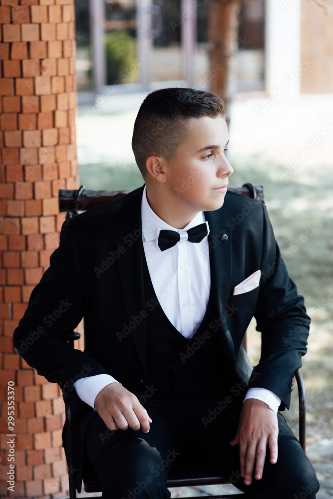 Handsome young boy with short hair wearing classic black suit and black bow  tie posing outdoor. Classic style. Stock Photo | Adobe Stock
