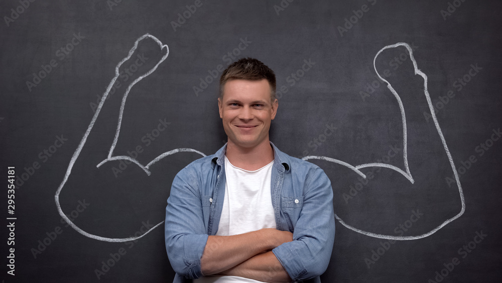 Smiling man with hands crossed standing against wall with muscled arms drowning