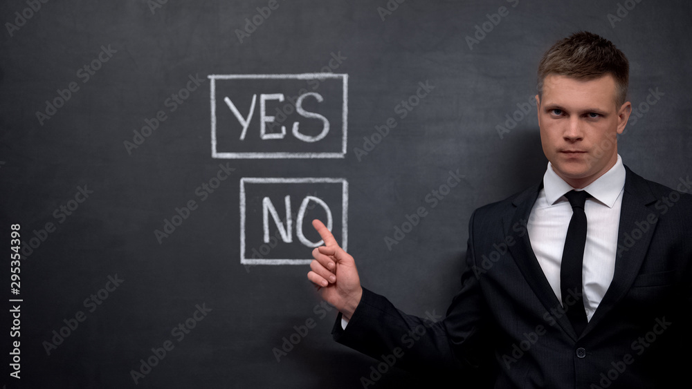 Serious man in suit pointing finger into no sign painted on blackboard, choice Serious man in suit pointing finger into no sign painted on blackboard, choice