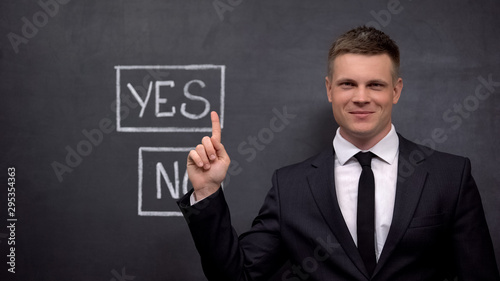 Smiling businessman showing yes button painted on blackboard, investment