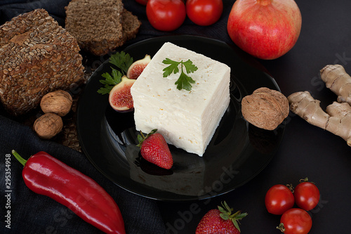 White luxury cheese, on a black plate, decorated with figs, dill and delicious strawberries, next to bread with cereals, walnuts and cherry tomatoes. The concept of cheese or healthy natural products.