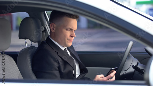Nervous man in suit sitting on driver seat and calling on phone, late for work