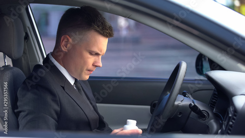 Man in business suit taking drugs in car, risk of side effects, dizziness © motortion