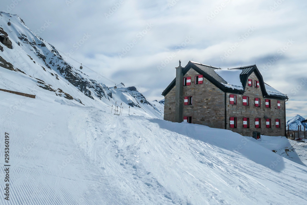 A big alpine cottage covered snow in Mölltaler Gletscher, Austria. Thick snow covers the surroundings. Clear weather. Perfectly groomed slopes. Beautiful and serene mountains covered with snow.